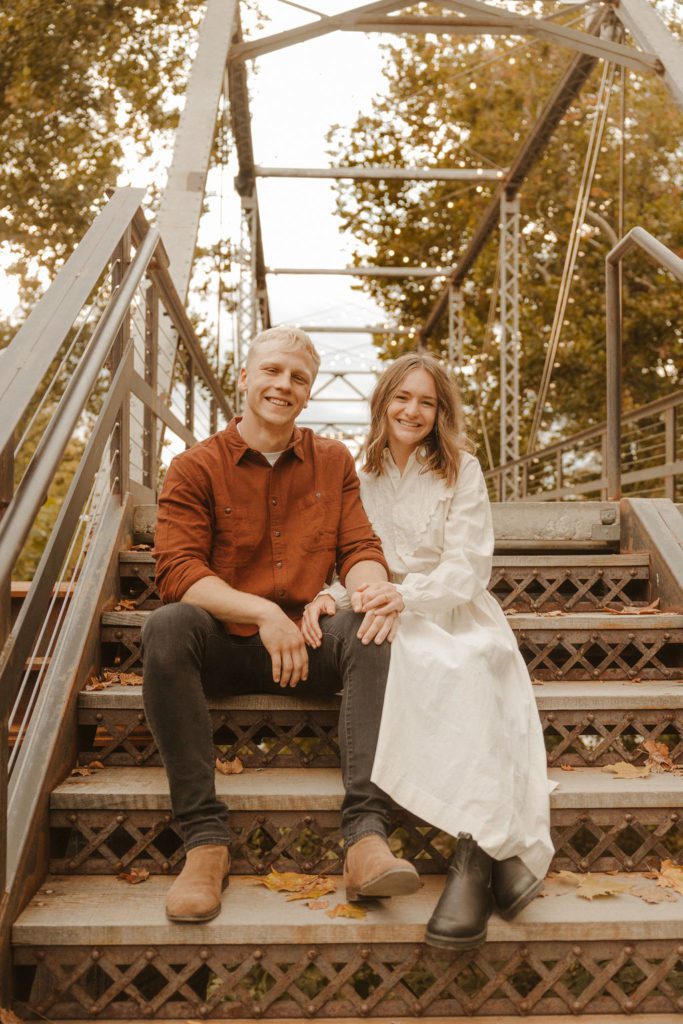 Newly engaged couple sitting on the steps of riverside bridge at finley farms in ozark missouri