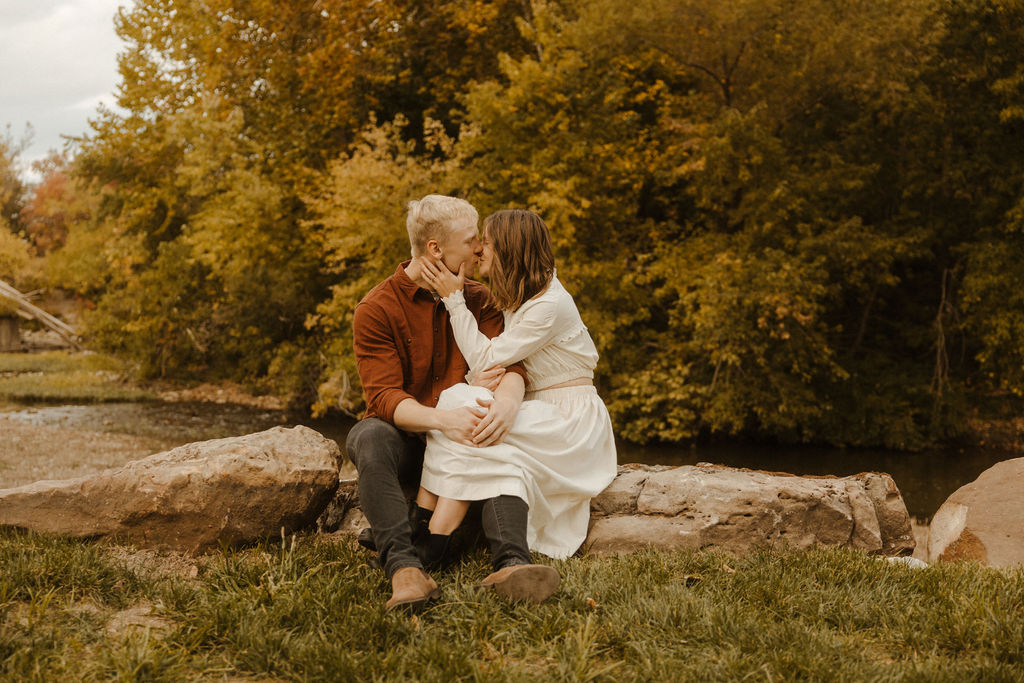 Newly engaged couple sitting on rocks kissing at Finley Farms in Ozark, Missouri