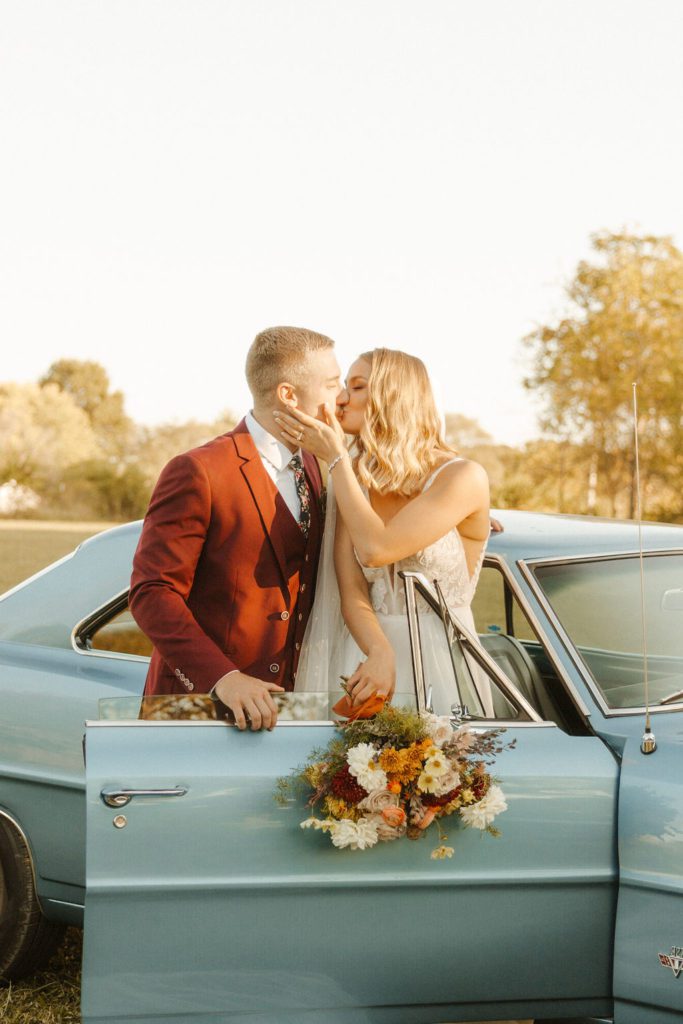 Newly wed couplekissing nextto a  vintage car 